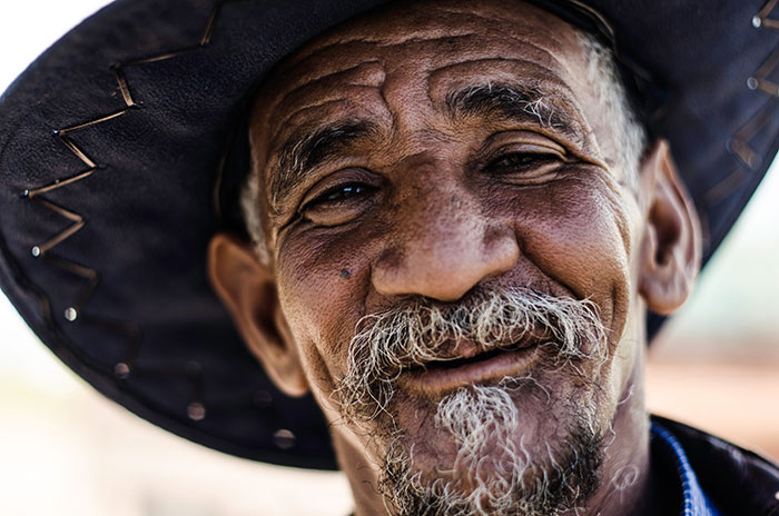 Close-up of an old man with a hat, smiling gently, illustrating wise funny and naughty advice from grandparents.