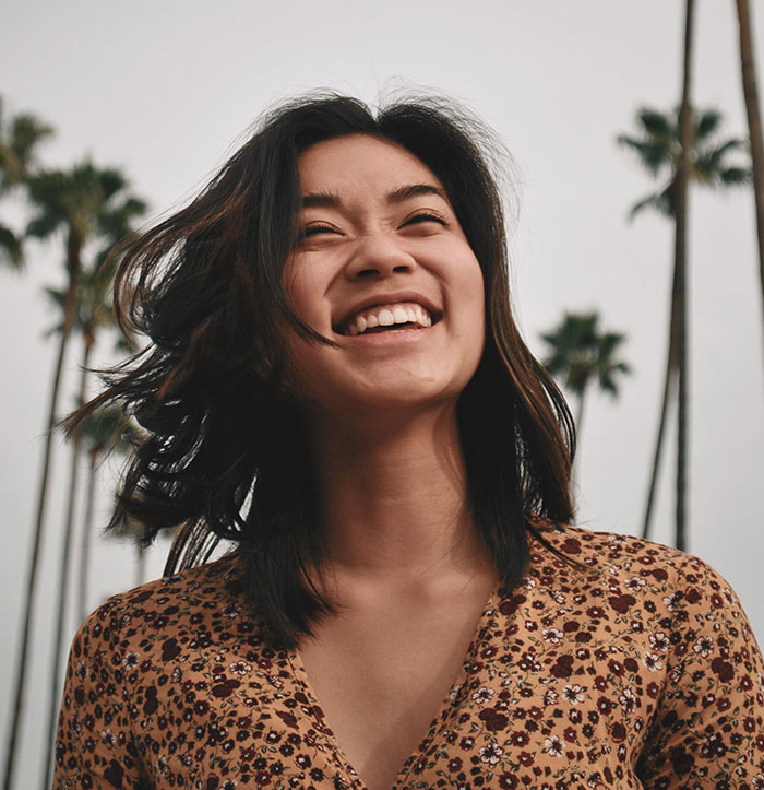 Smiling woman outdoors with palm trees, radiating joy inspired by wise funny and naughty advice from grandparents.