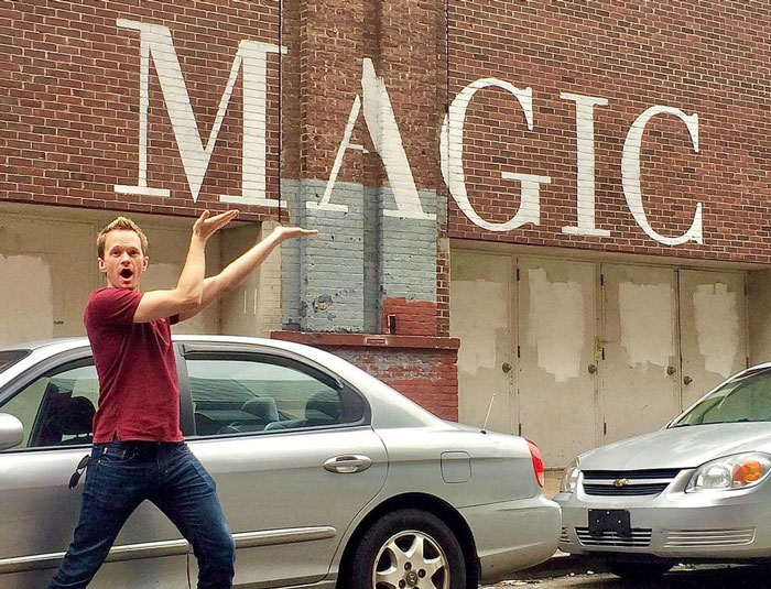 Neil Patrick Harris posing funny next to a writing on the wall 