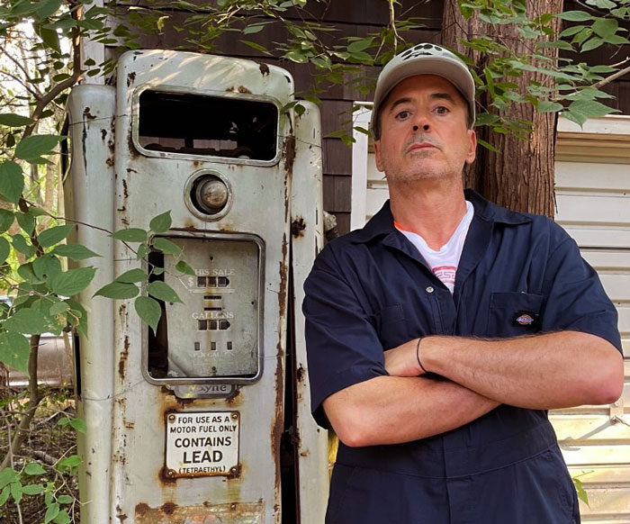 Robert Downey Jr standing next to a abandoned gas station with crossed hands 