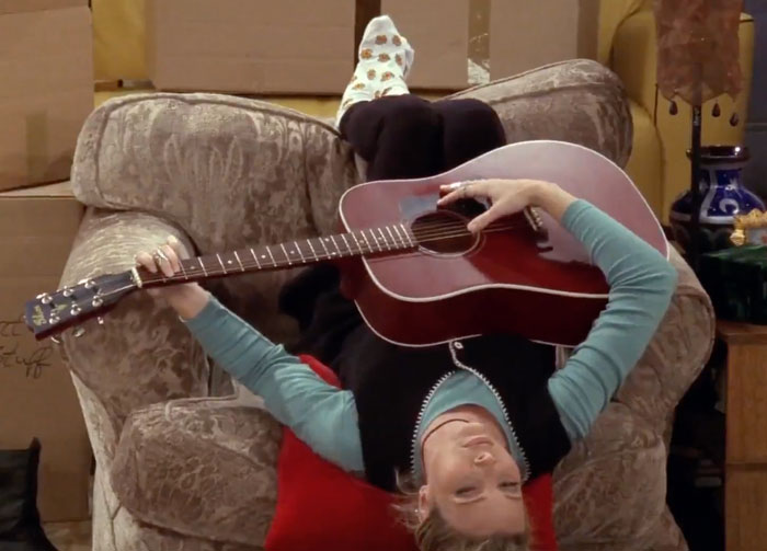 Phoebe playing the guitar upside down on the chair 