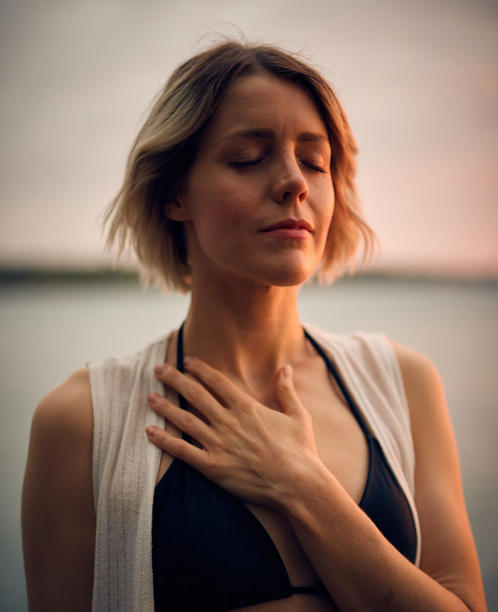 Woman with closed eyes holding a hand on her heart 
