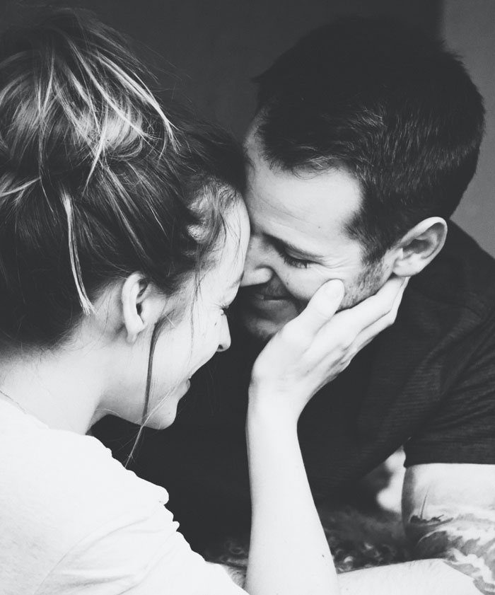 Woman holding hands on man's face and both are smiling 