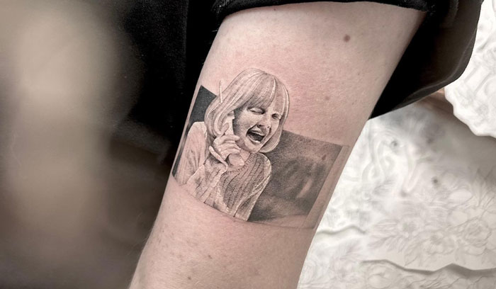 Person with detailed pop culture tattoo on arm, depicting a black and white illustration of a laughing woman.