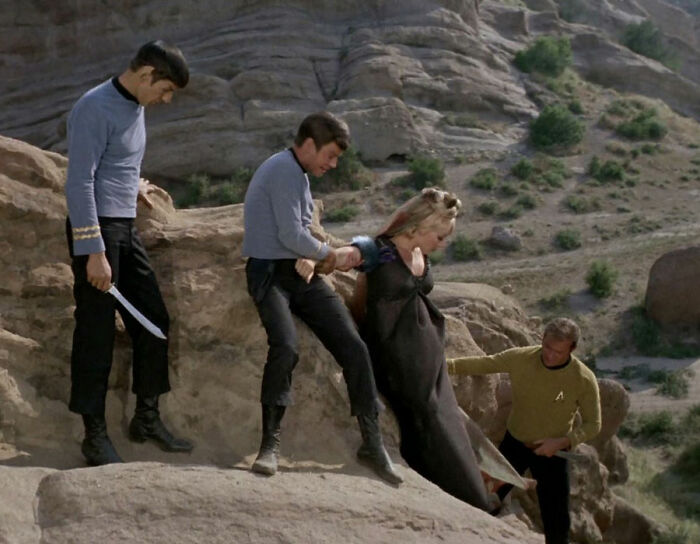 Crew members helping a lady down a rock