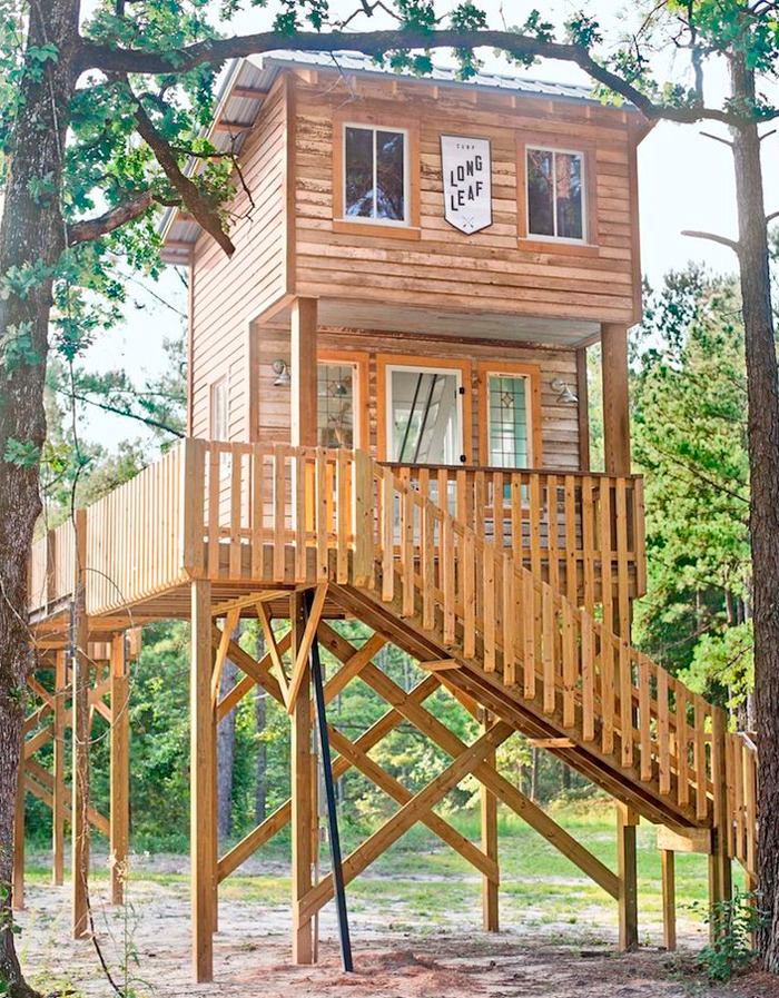 Elevated tiny house design with wooden exterior and staircase in a forest setting.