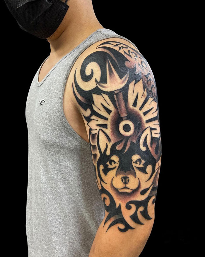 Arm with intricate tribal tattoo featuring abstract shapes and a wolf design, on a person wearing a gray tank top.