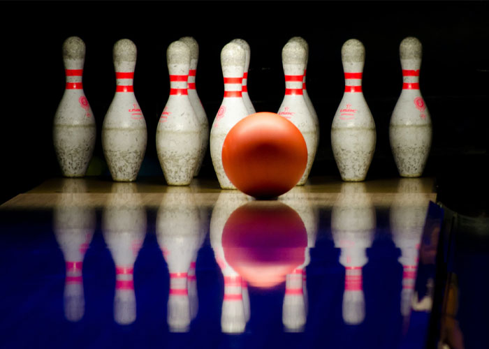 Bowling ball rolling towards seven white pins with red stripes, illustrating unique college courses concept.