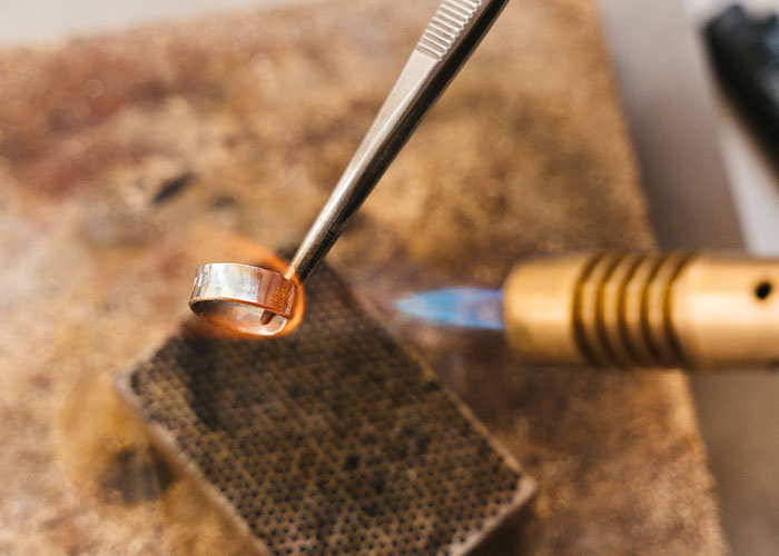 Close-up of metalworking in a college course, heating a ring with a blowtorch in a workshop setting.