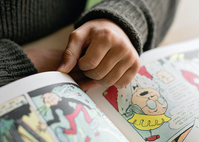 Person flipping through a colorful comic book, exploring unique college courses that you probably never knew existed.