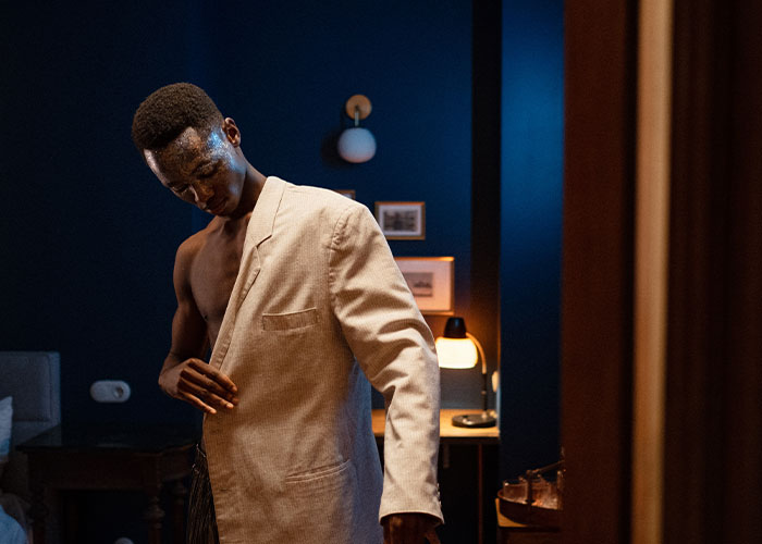 Young man trying on a beige jacket in a dimly lit room, representing unique college courses concept.
