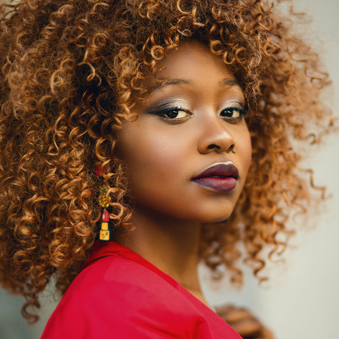 Young woman with curly hair wearing red, looking confidently at camera, representing unique college courses idea.