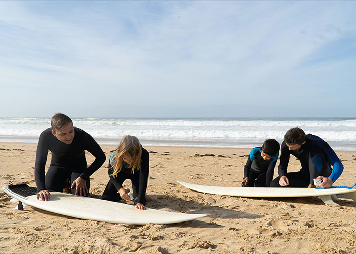 Four people on the beach preparing surfboards, illustrating unique college courses in practical outdoor skills.