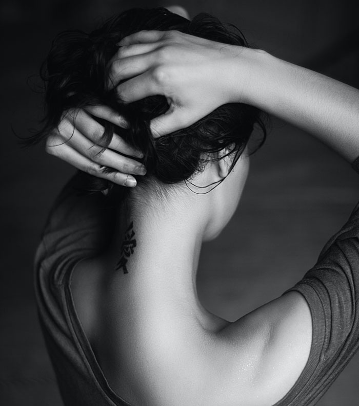 Person with a neck tattoo, hair pulled back, in grayscale.