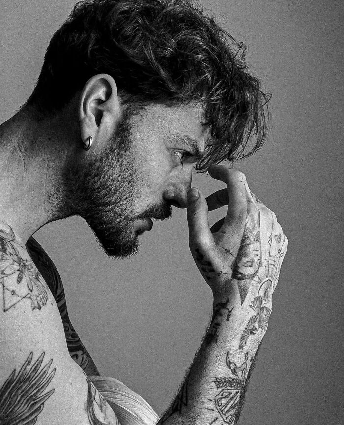 Profile of a tattooed man touching his face, showcasing geometric tattoo style on arms. Profile of a tattooed man touching his face, showcasing geometric tattoo style on arms.