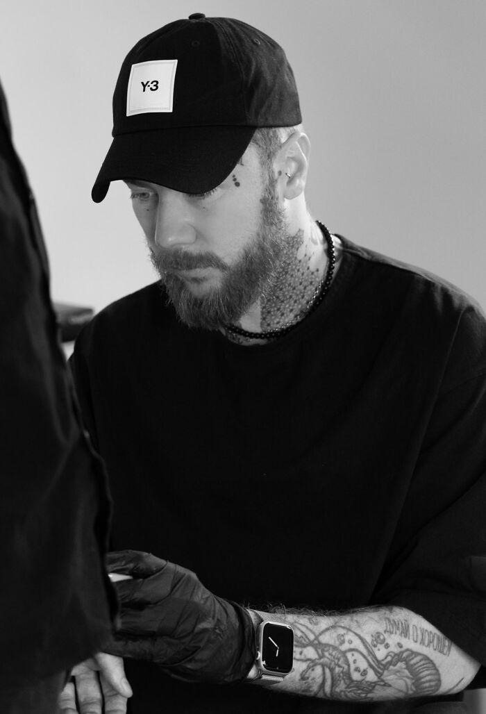 Tattoo artist focused on intricate geometric design, wearing a cap and gloves, showcasing detailed arm tattoos. Tattoo artist focused on intricate geometric design, wearing a cap and gloves, showcasing detailed arm tattoos.