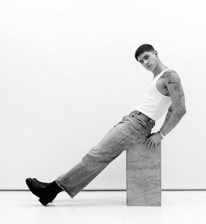 Person in a white tank top and jeans, showcasing geometric tattoos in a minimalist setting. Person in a white tank top and jeans, showcasing geometric tattoos in a minimalist setting.