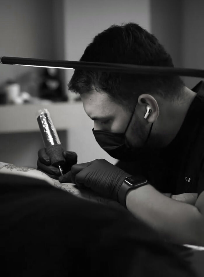 Tattoo artist focused on creating a geometric tattoo, wearing a mask and gloves, holding a tattoo machine. Tattoo artist focused on creating a geometric tattoo, wearing a mask and gloves, holding a tattoo machine.