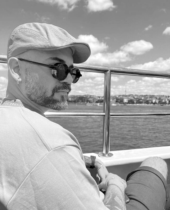 Man with beard and sunglasses on a boat, showcasing geometric tattoo style, ocean and cityscape in the background. Man with beard and sunglasses on a boat, showcasing geometric tattoo style, ocean and cityscape in the background.