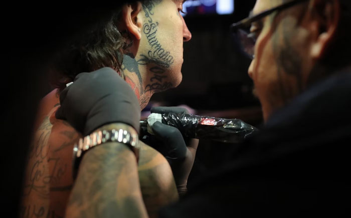 Tattoo artist working on client's neck and back in dimly lit setting.