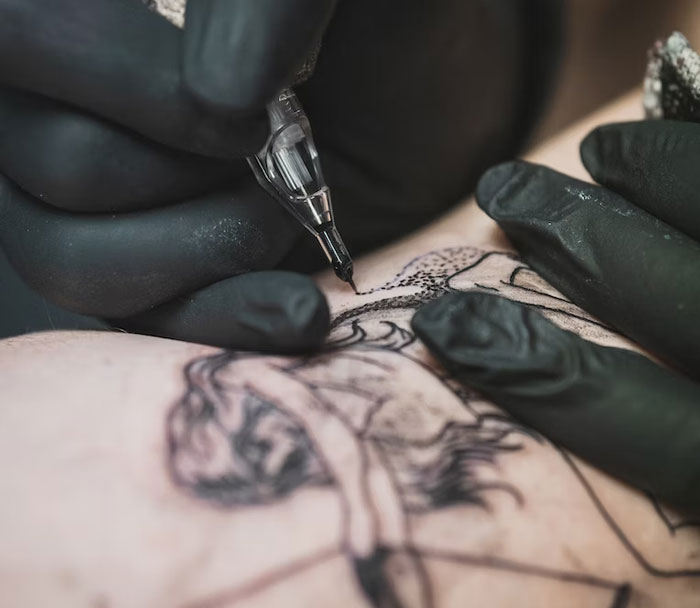 Tattoo being inked on a person's arm with a detailed design by an artist in black gloves.