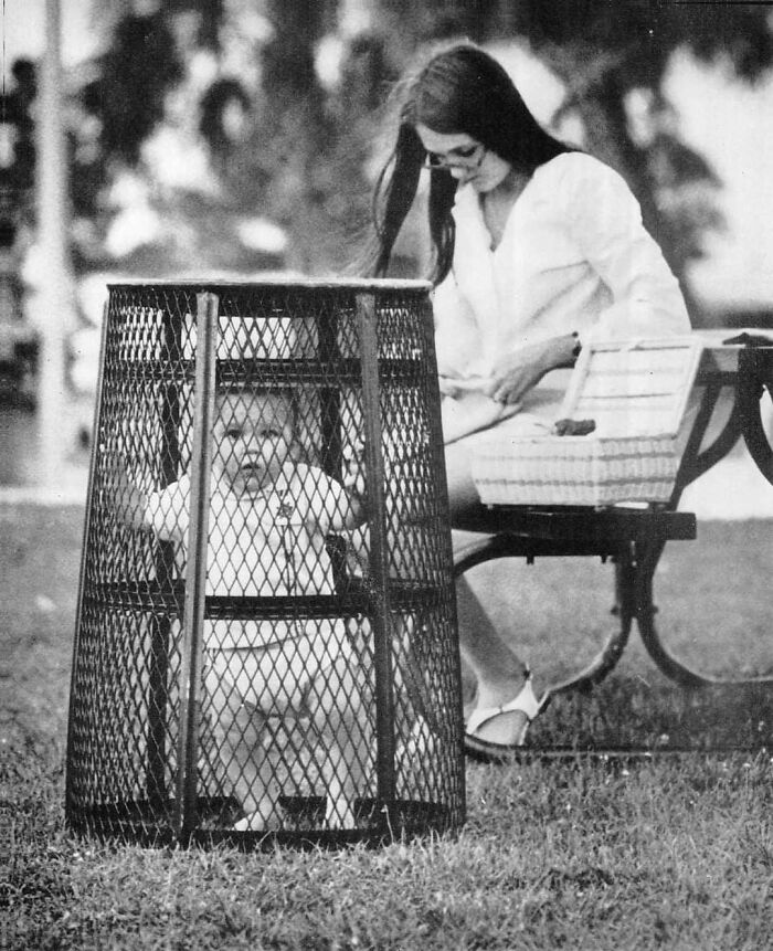 A Mom Uses A Trash Can To Contain Her Baby While She Crochets In The Park, 1969