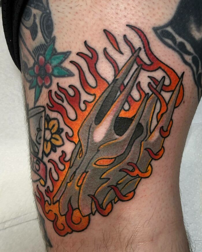 "Vibrant flaming helmet tattoo inspired by Lord of the Rings on upper arm, featuring detailed orange and red flames."