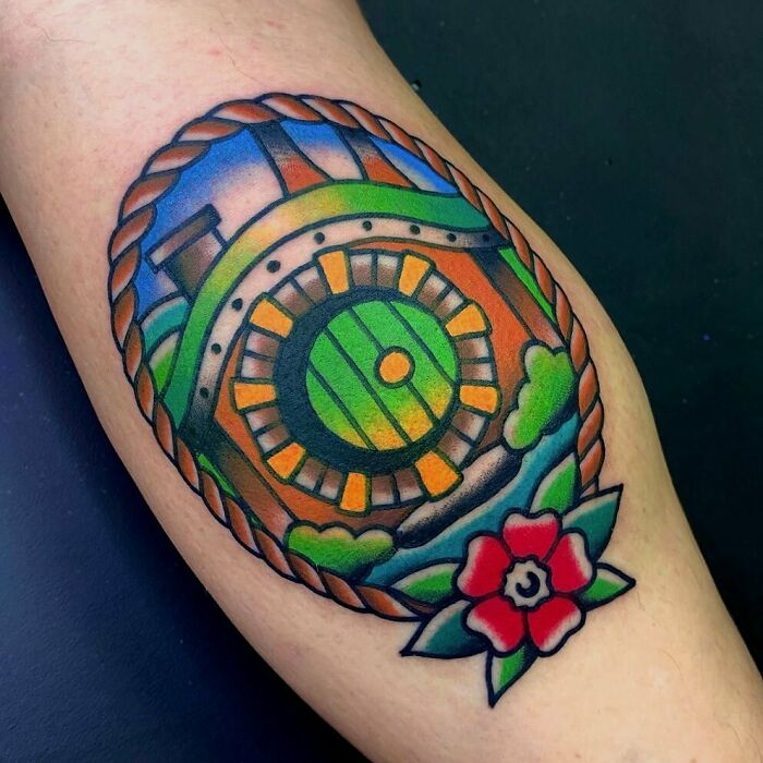 Colorful Lord of the Rings tattoo featuring a Hobbit door with vibrant greenery and a red flower.