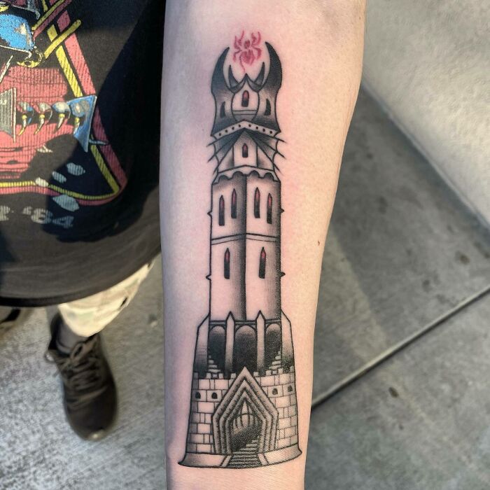 Tattoo of Saruman's tower from Lord of the Rings on forearm, with detailed black and red ink design.