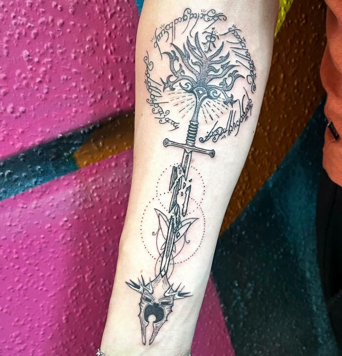 Stylized Lord of the Rings tattoo with sword, Elvish script, and ornate designs on forearm.