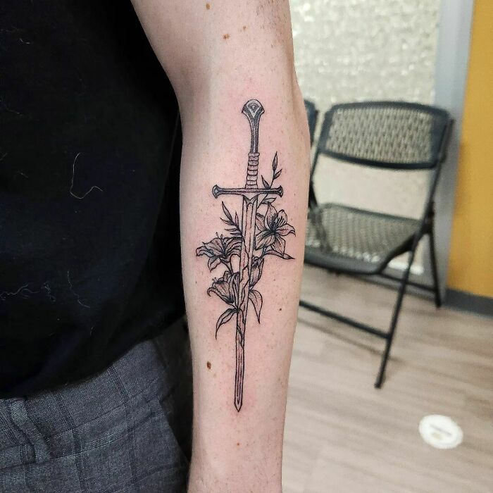 "Lord of the Rings tattoo of a sword entwined with flowers on a person's forearm."