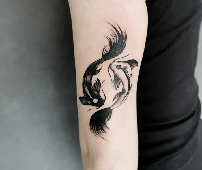 Zodiac tattoo of yin-yang koi fish on a person's forearm, intricate and bold design.