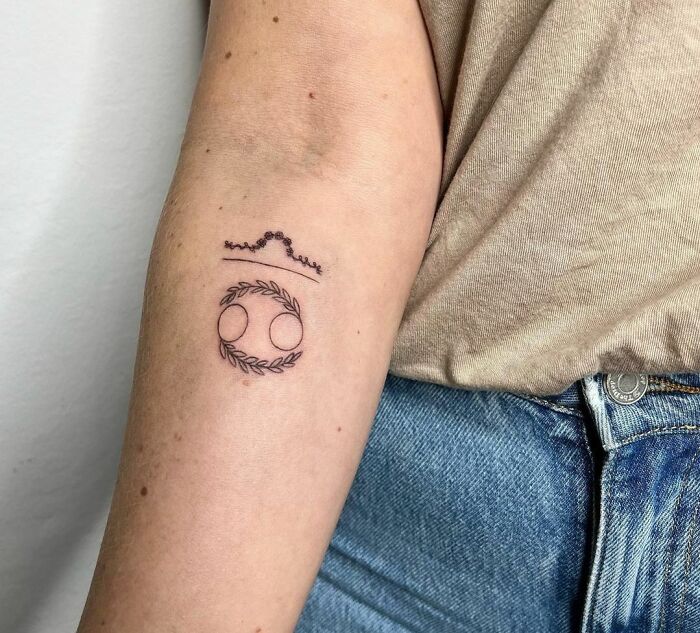 Minimalist zodiac tattoo on arm with intricate line art design above blue jeans.