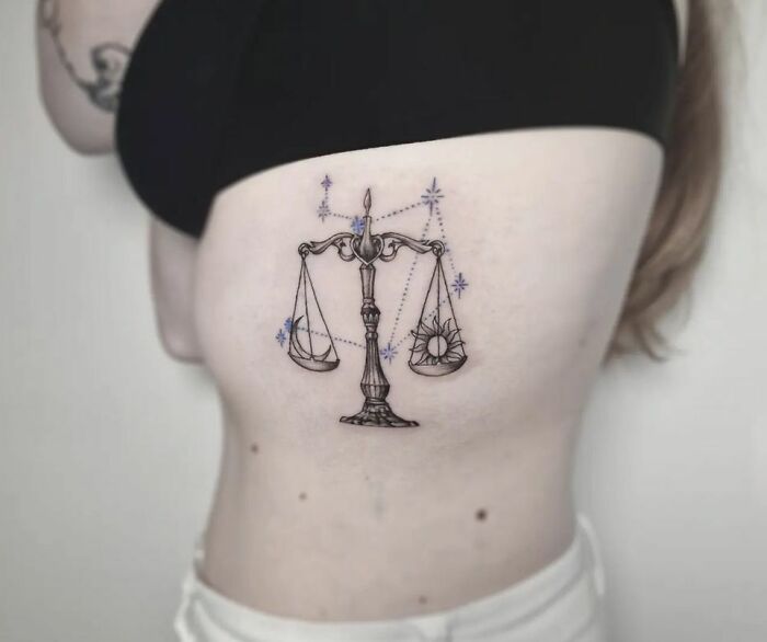 Libra zodiac tattoo on a person's side with scales and constellation details.
