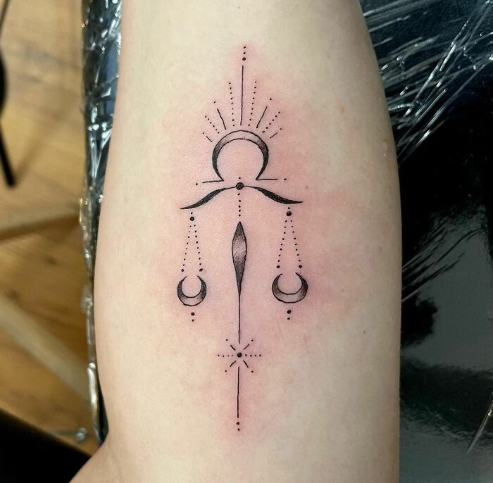 Elegant zodiac tattoo with abstract lines and dots on an arm.