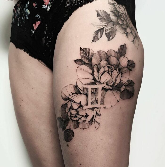Gemini zodiac tattoo with intricate floral design on woman's thigh.
