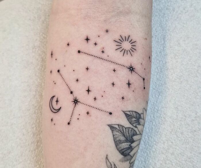 Minimalist zodiac tattoo featuring constellations with stars, moon, and sun elements on arm.