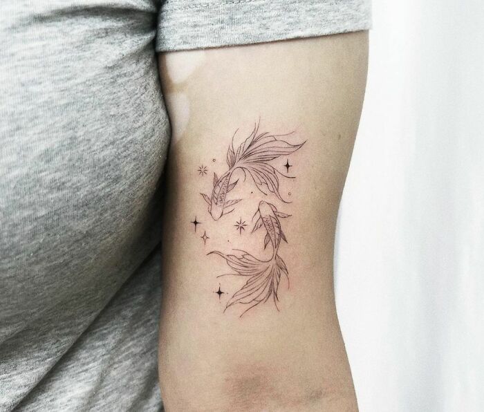 Zodiac tattoo on arm featuring two Koi fish and stars, symbolizing Pisces.