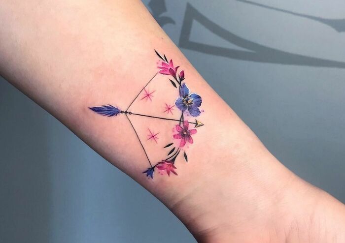 Colorful Zodiac tattoo of a constellation adorned with pink and blue flowers on forearm.