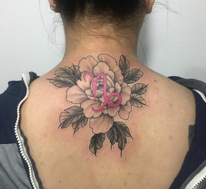 Zodiac tattoo featuring a pink Capricorn symbol over a large floral design on the upper back.