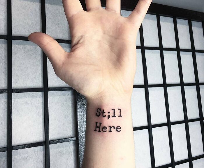 "Still here" phrase and semicolon wrist tattoo 
