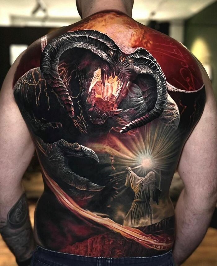 A detailed Lord of the Rings tattoo depicting a battle scene with a dragon and wizard on a man's back.