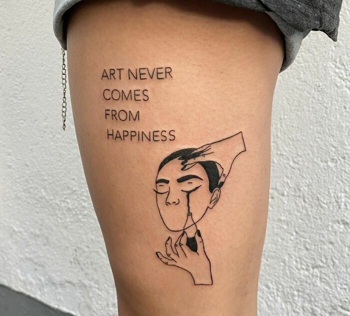 "Art Never Comes From Happiness" and sad face leg tattoo 
