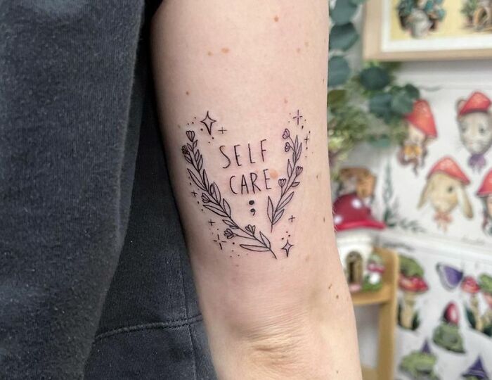 "self care" inscription next to plants and stars tattoo
