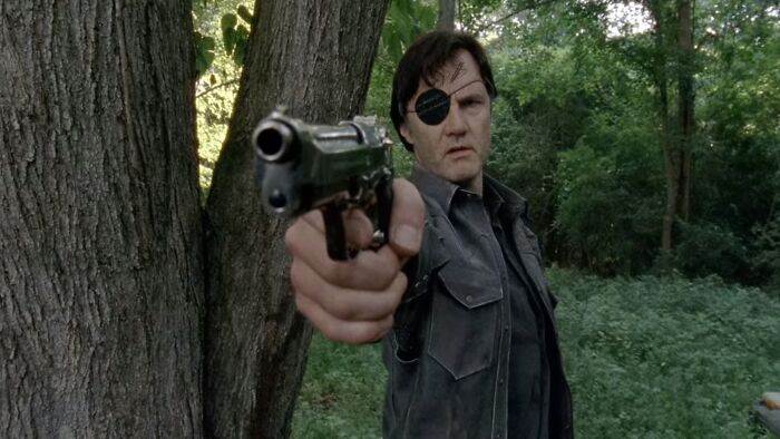 The Governor holding a gun in the forest