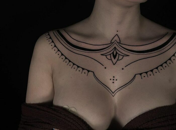 Close-up of a woman's chest featuring an intricate tribal tattoo design in black ink.