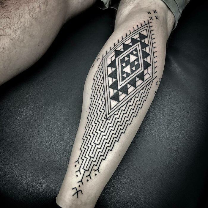 Geometric tribal tattoo design on a person's calf, featuring intricate black patterns and shapes.