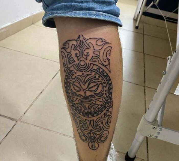 Tribal tattoo design on calf with intricate patterns and mask motif.