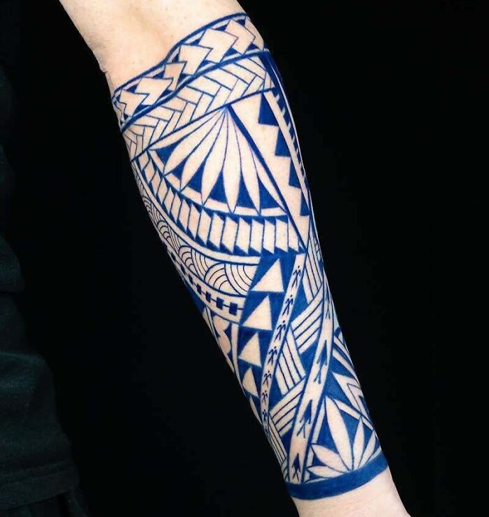 Forearm with intricate blue tribal tattoo design featuring geometric patterns.