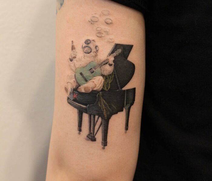 Realistic tattoo of a deep sea diver sitting on piano, holding guitar and a drink